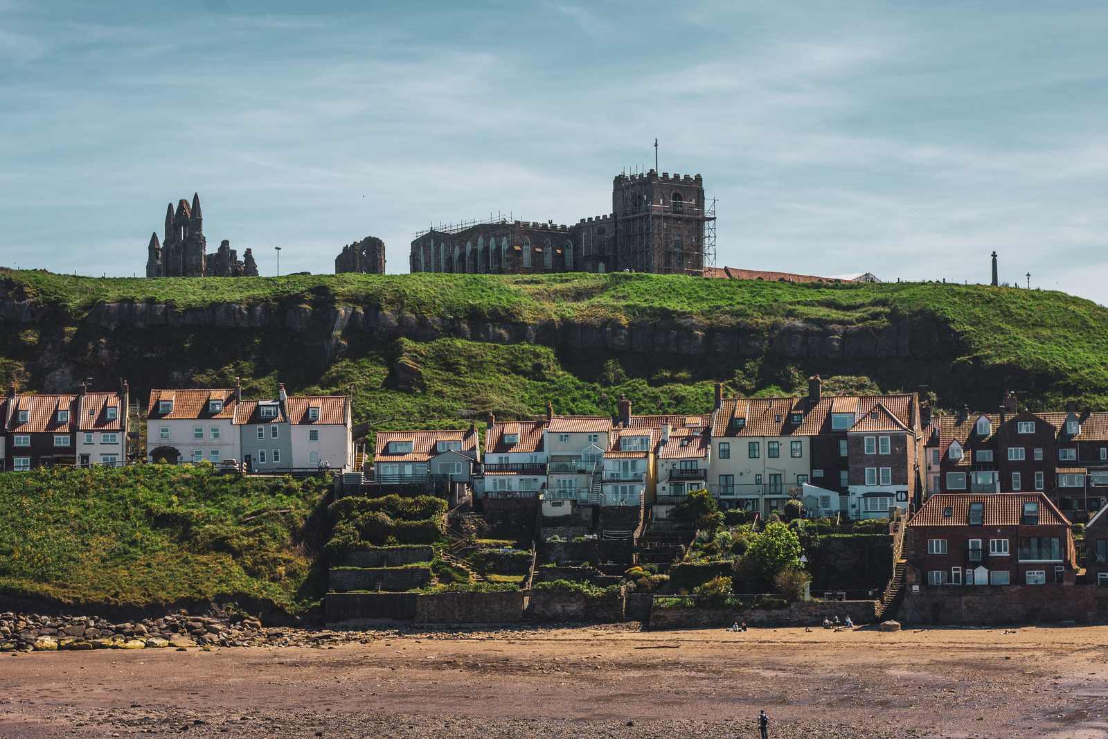Houses built into a cliff face above a beach, with a large building on the cliff top