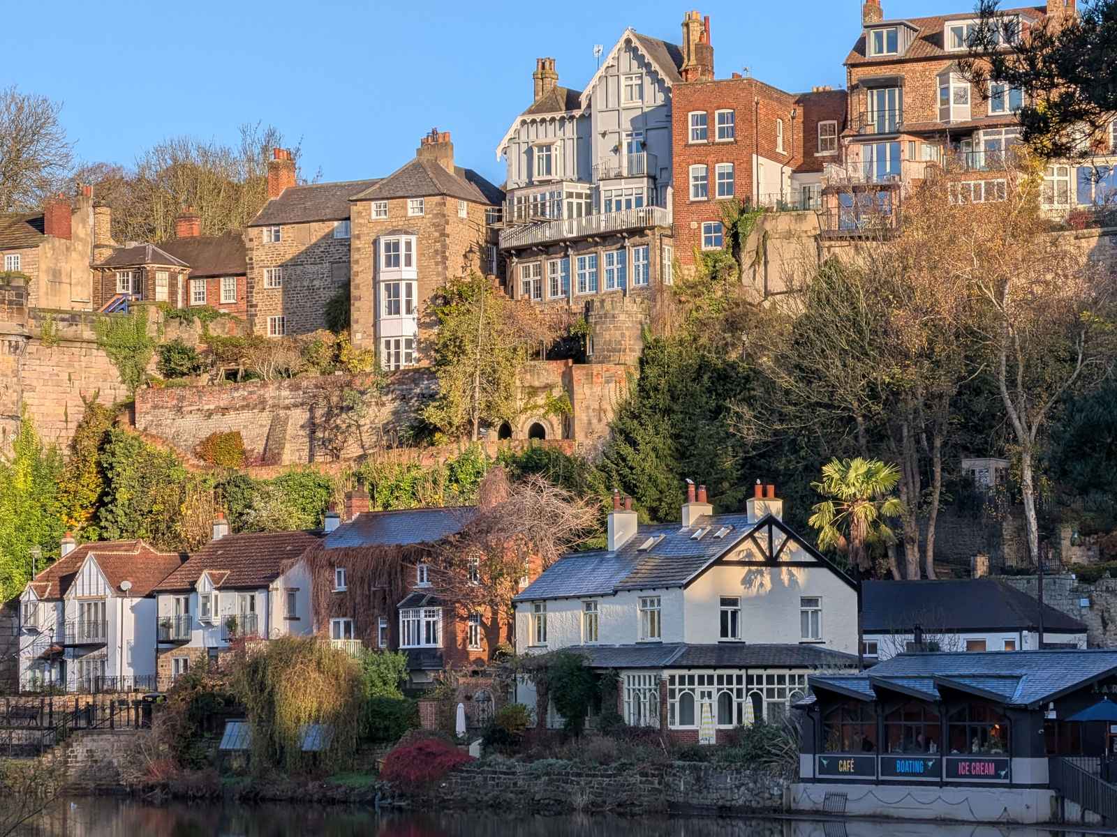 Houses built on a steep hillside overlooking a river, with various architectural styles and materials