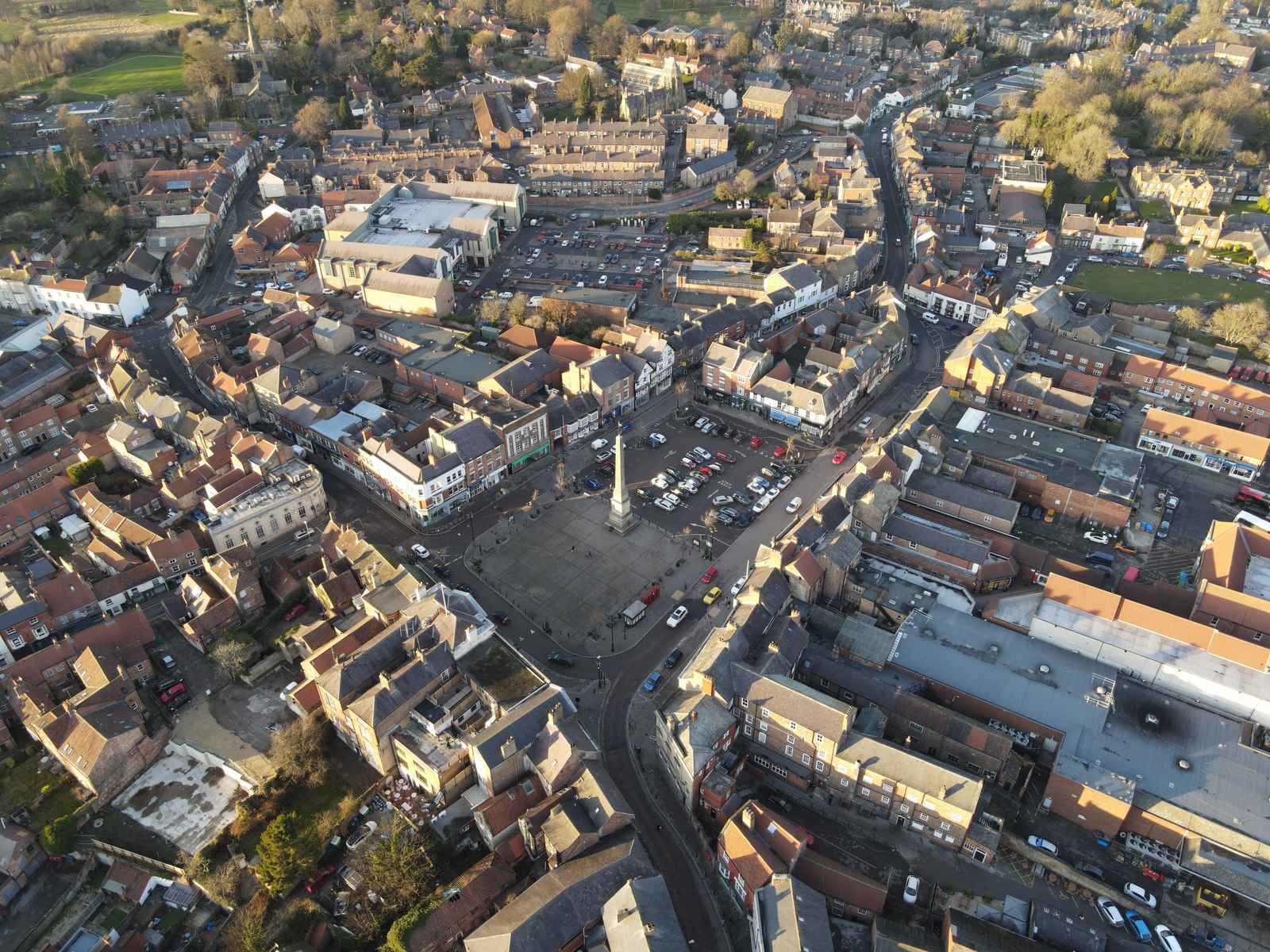 An aerial view of a town centre with buildings, roads, and a central square with a monument